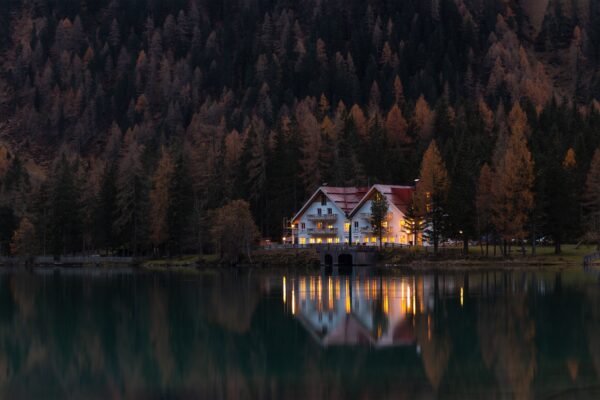 Una scena invernale serena di una baita illuminata che si riflette in un lago tranquillo durante il crepuscolo.